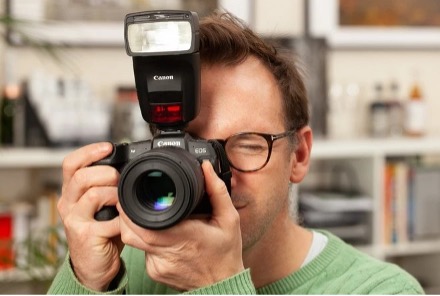 Man holding a canon camera with Speedlite flash attached