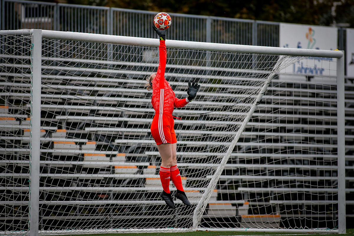 female goalie reaching for a high flying soccer ball