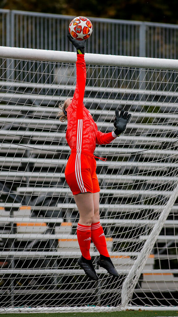 female goalie reaching for a high flying soccer ball