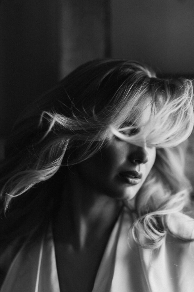 A black and white portrait of a woman with wavy hair blowing across her face.